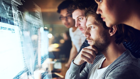 A group of employees looking at the data feeds on the big monitor
